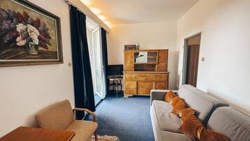 Ein gemütlicher Wohnbereich mit Sofa, Sessel, kleinem Tisch, Schrank und einem Bild an der Wand.