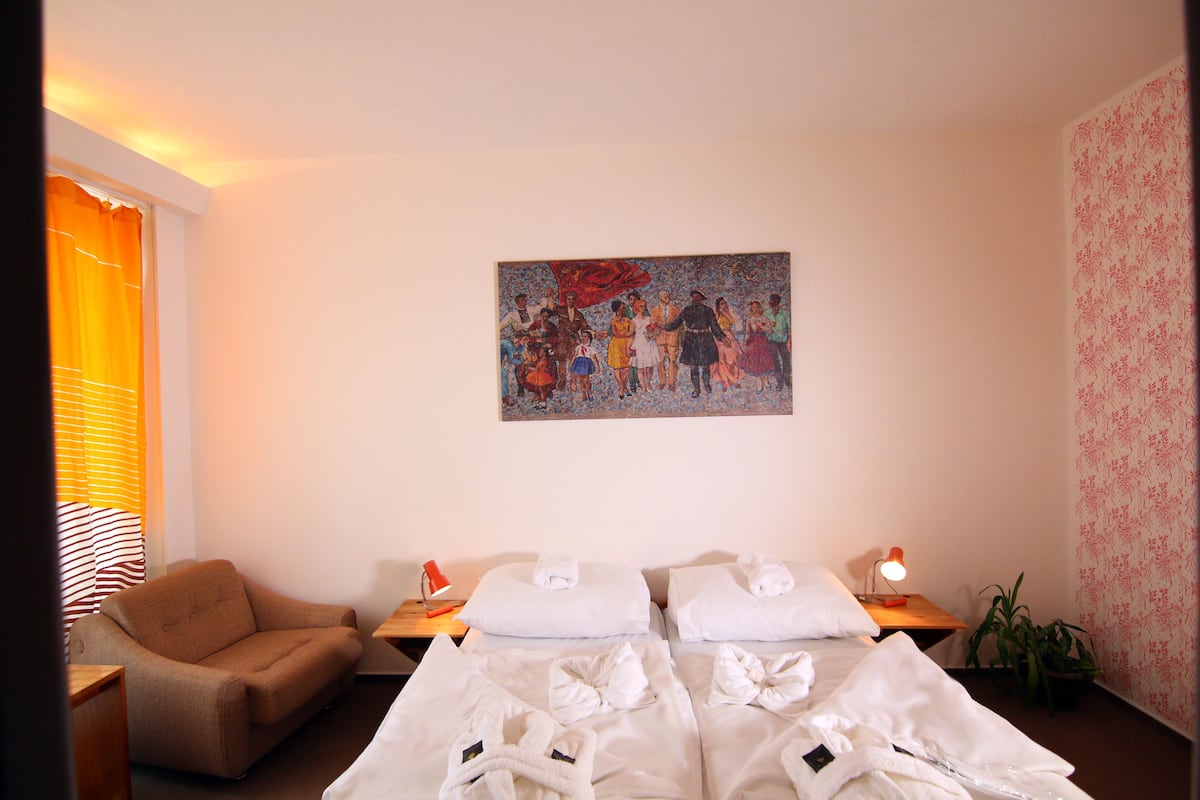 A hotel room with two beds, a sofa, a painting, and a window with curtains.