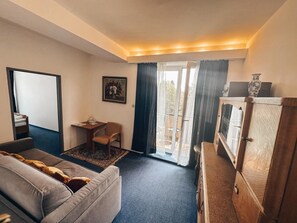 A hotel room with a sofa, a small table with a chair, a cabinet, and a view of the outdoors through a glass door. - Hotel Medlov (Frysava pod Zakovou horou)