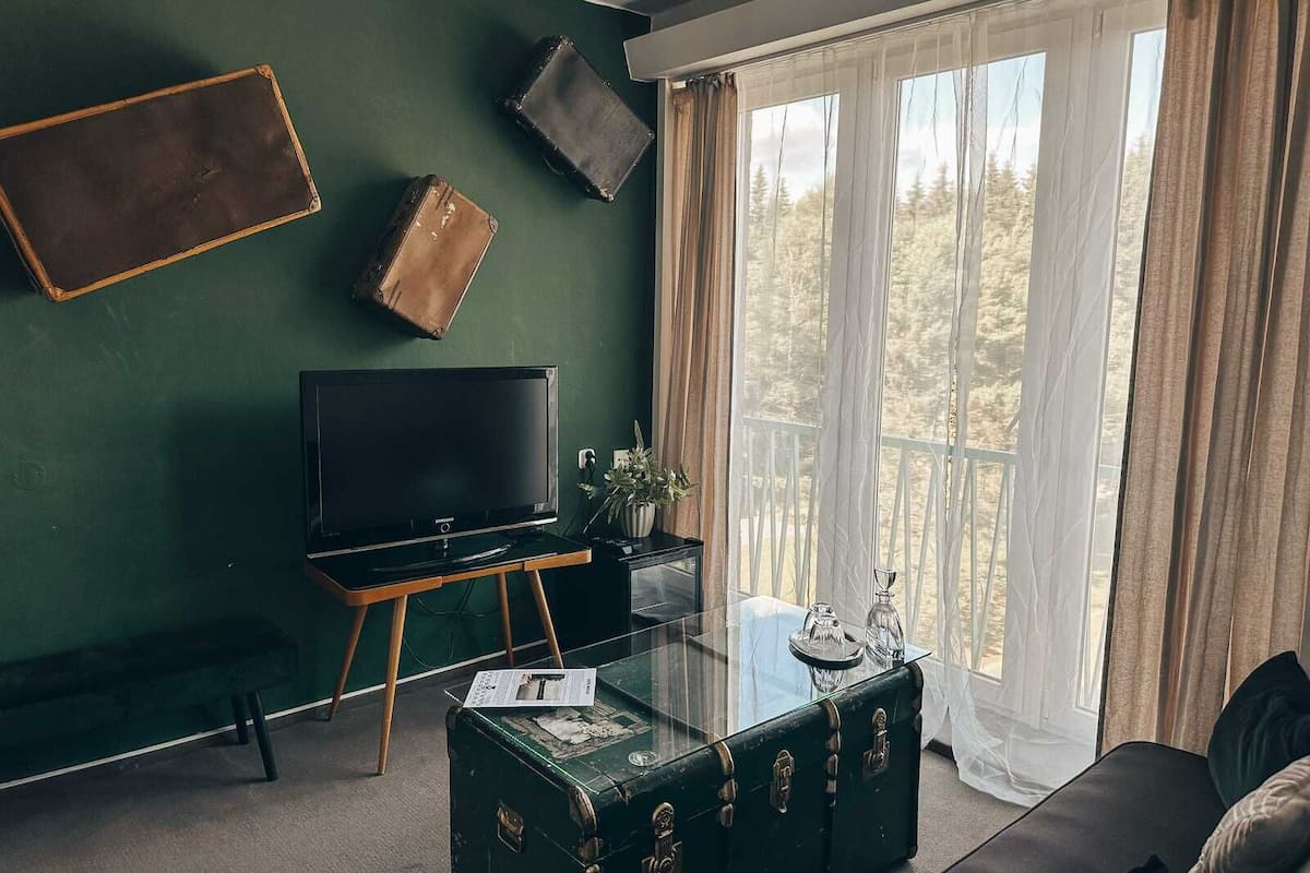 A living room with a green wall, a television, a glass coffee table, and a window with curtains.