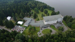 An aerial view of a large building surrounded by a forested area and a lake. - Hotel Medlov (Frysava pod Zakovou horou)