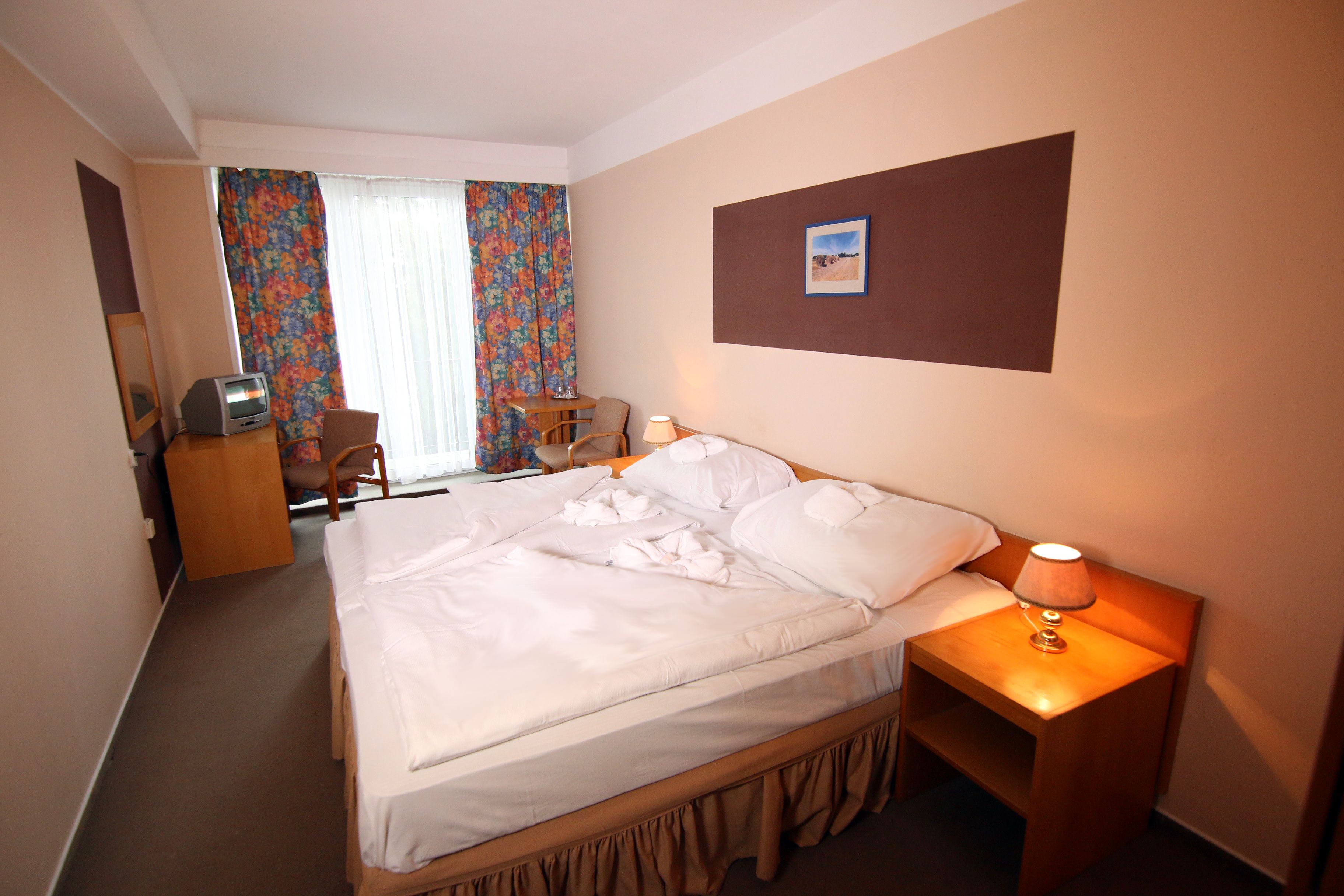 Ein Hotelzimmer mit Bett, Schreibtisch, Stuhl, Lampe und einem Bild an der Wand.
