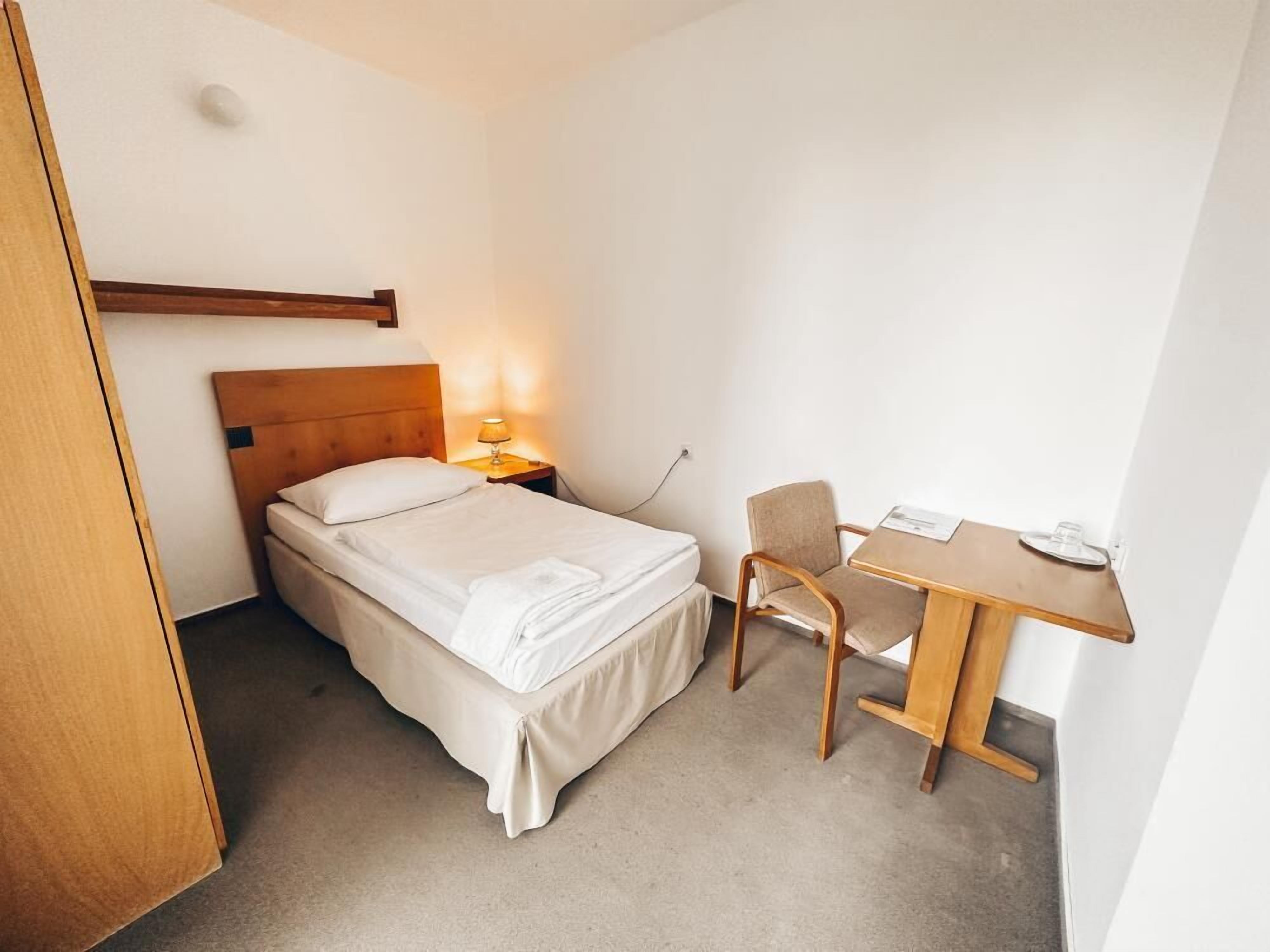 A hotel room with a bed, bedside table, chair, and desk.