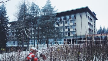 A multi-story building with balconies, surrounded by trees and snow-covered ground.