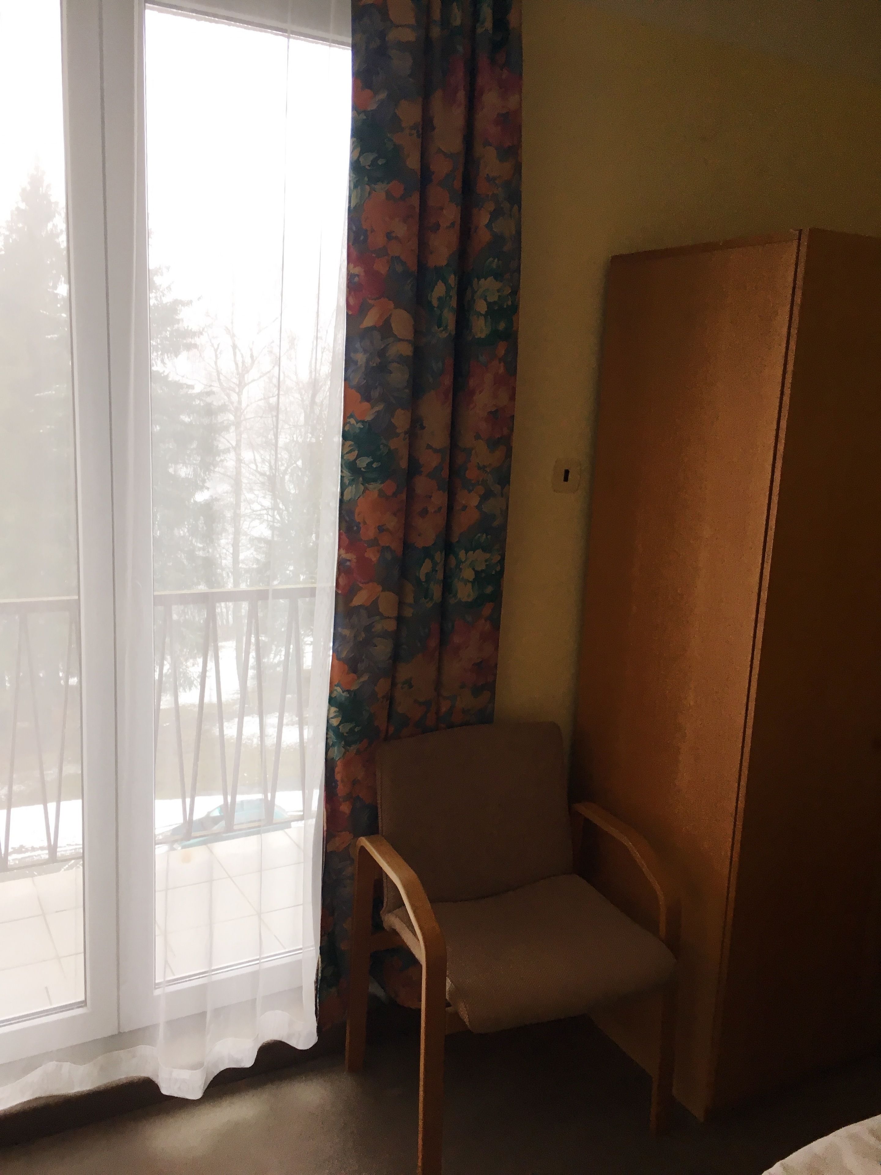 Una habitación con un ventanal grande, una silla y un armario de madera.