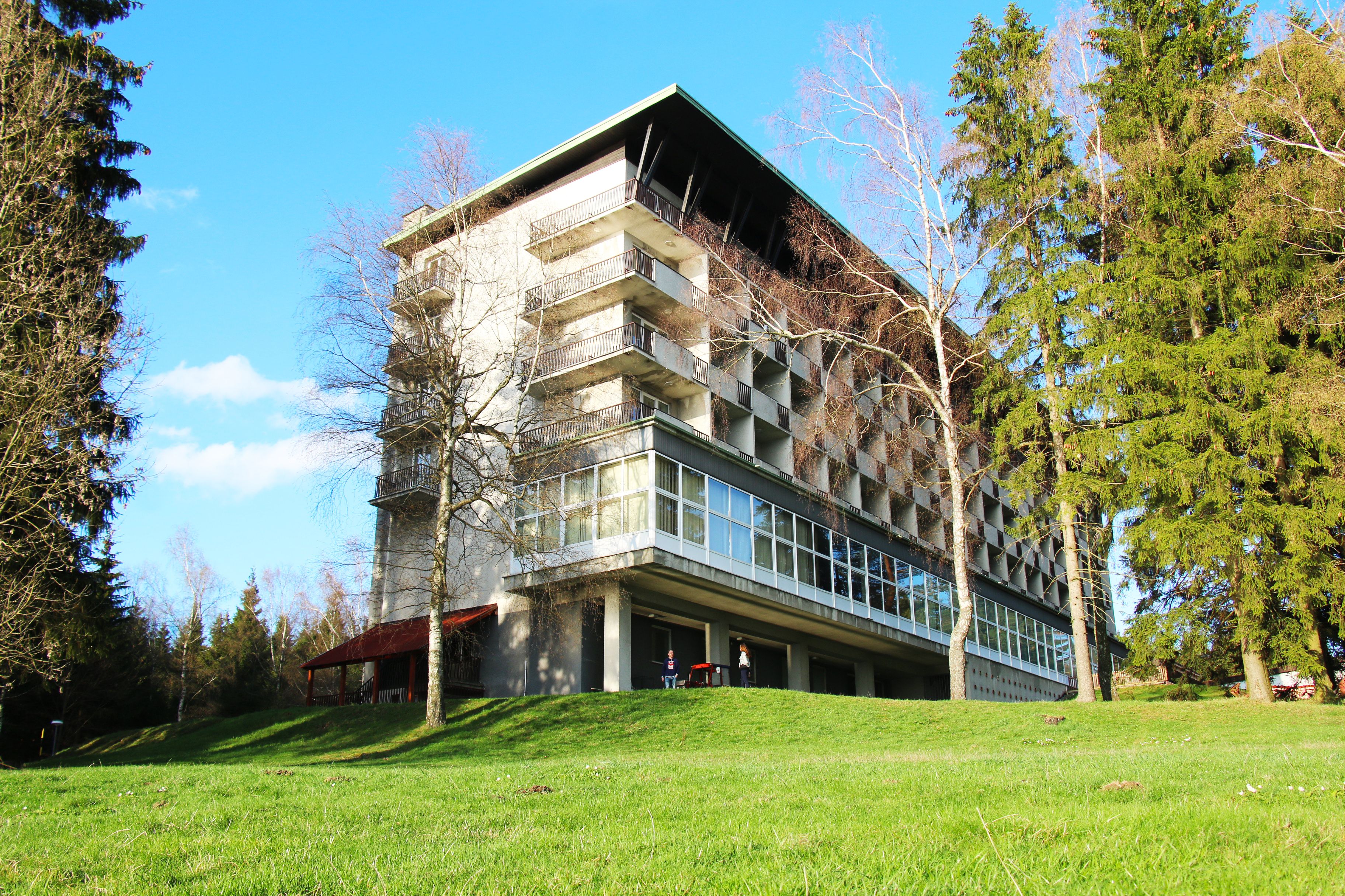 A modern building with a flat roof and large windows, surrounded by trees and a grassy area.