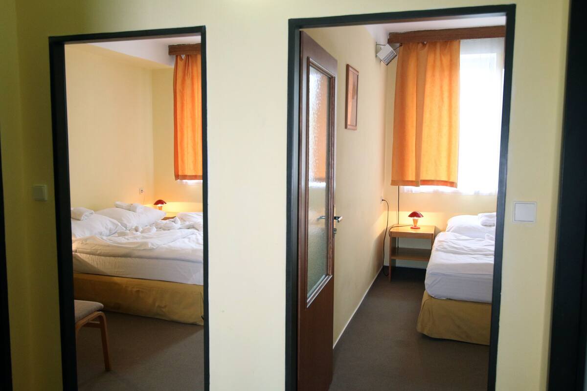A hotel room with two beds, a chair, and a nightstand with a lamp.