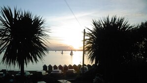 Une vue sur la plage, avec des palmiers, des tables de pique-nique et un coucher de soleil sur l’eau.