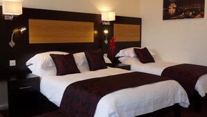 Une chambre d’hôtel avec deux lits, des têtes de lit en bois foncé, du linge de lit blanc et une table de chevet avec une lampe.
