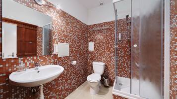 Un baño con salpicadero de azulejos, un lavabo, un inodoro y una ducha con mampara de cristal.