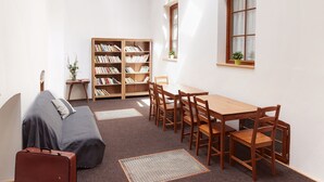 A room with a high ceiling, skylights, a wooden table with chairs, a bookshelf, a sofa, and a suitcase. - Ski Hotel Svoboda nad Upou (Svoboda nad Upou)