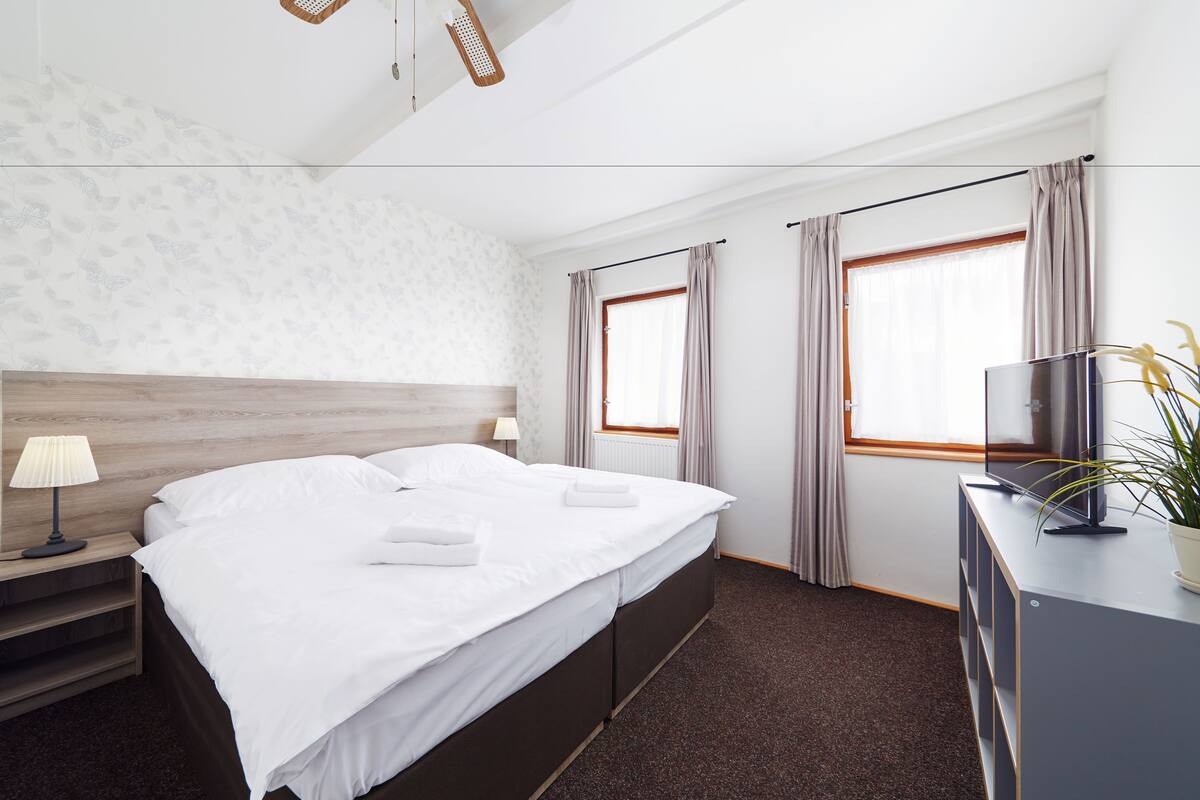 Une chambre d’hôtel avec un grand lit, des tables de chevet, une télévision et une fenêtre avec des rideaux.