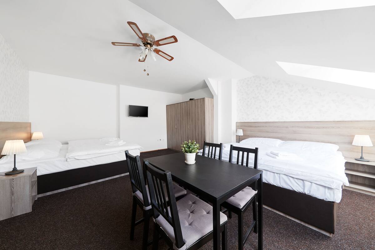 Une chambre d’hôtel équipée d’un lit, d’un bureau, d’une chaise, d’une table, d’un ventilateur de plafond et d’un téléviseur.
