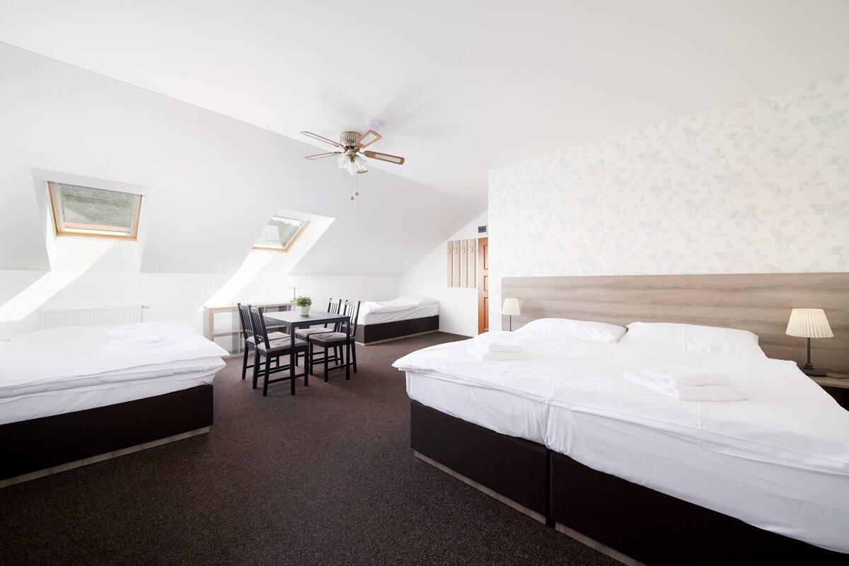 Une chambre d’hôtel avec deux lits, un ventilateur de plafond, une petite table avec des chaises et une fenêtre.