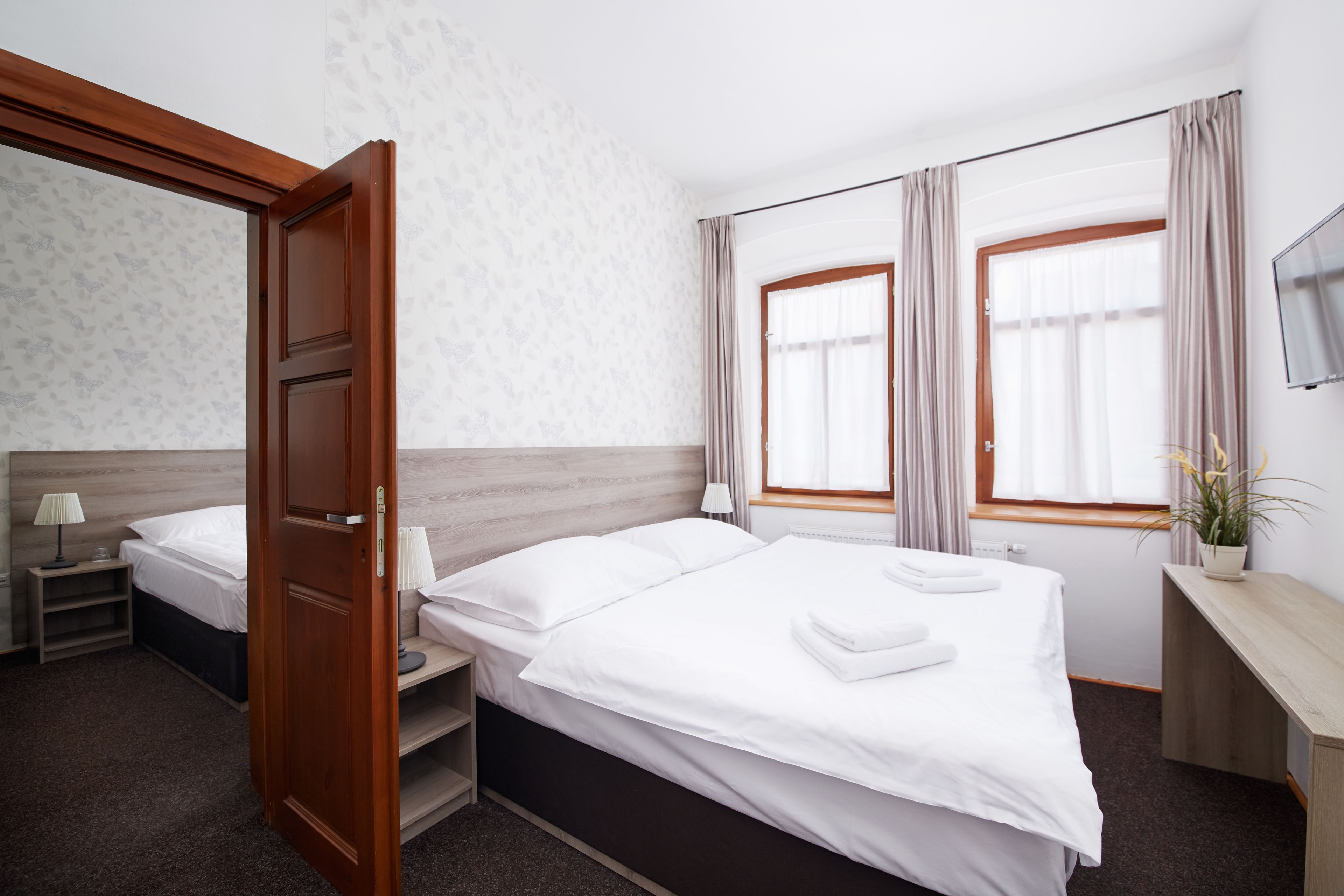 Una habitación de hotel con cama, mesitas de noche, televisión y ventanas con cortinas.