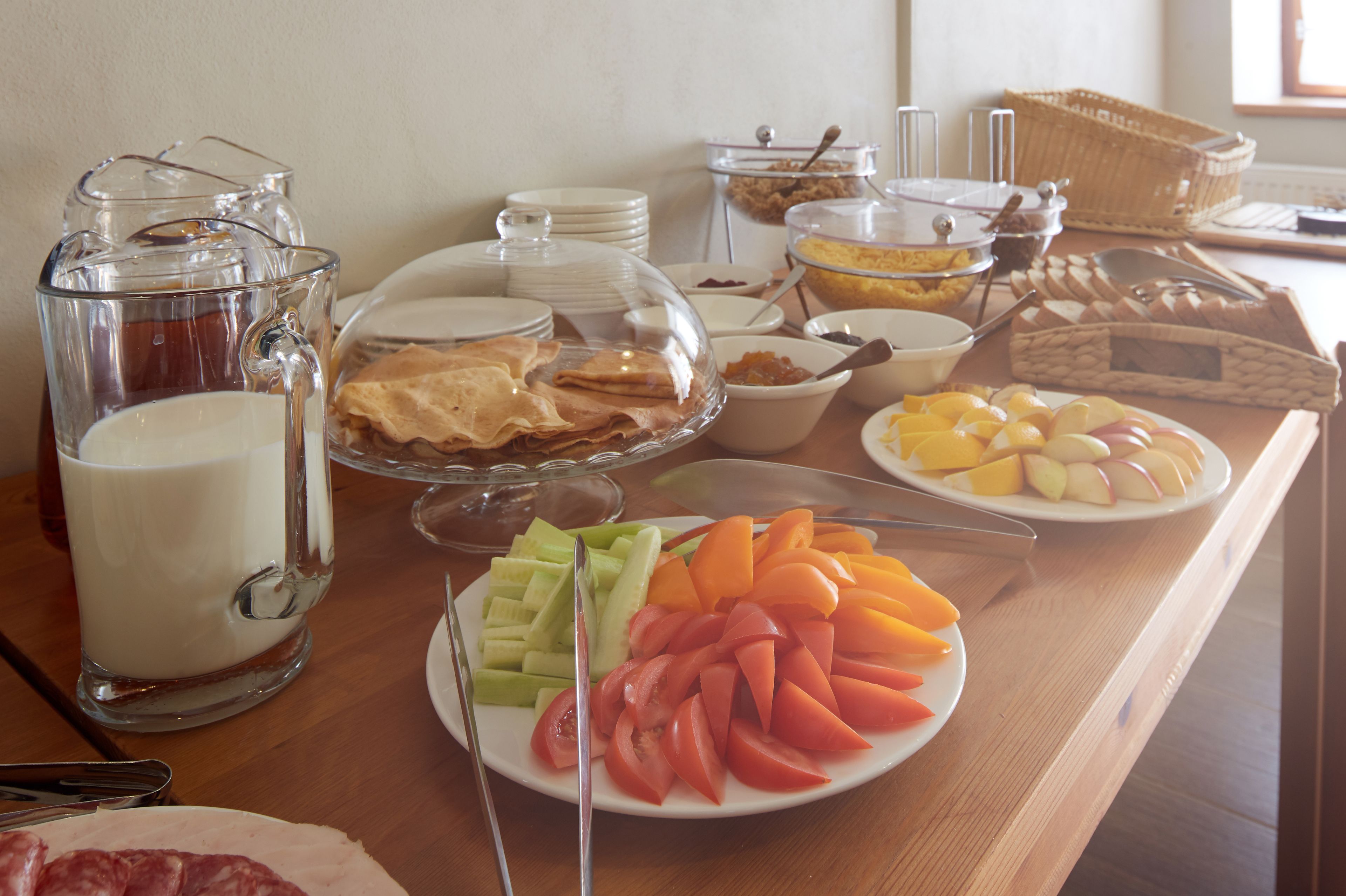 A buffet table with various food items, including fruits, pastries, and a milk jug.