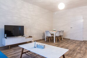 Une chambre moderne avec un téléviseur à écran plat posé sur une console blanche, une table à manger avec des chaises et un plancher en bois.