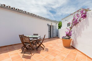 A patio with a table and chairs, a potted plant, and a white wall with a door. - Molino de Saladilla (Coin)