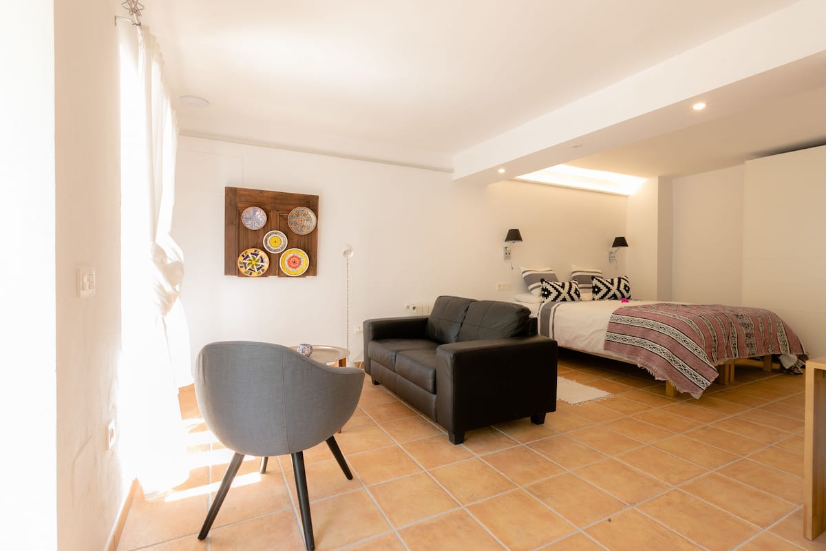 A modern bedroom with a bed, a sofa, a chair, and a wall with decorative plates.