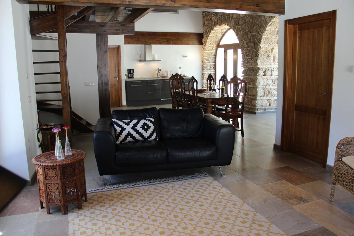 A living room with a black leather sofa, a patterned rug, and a small wooden side table with vases.