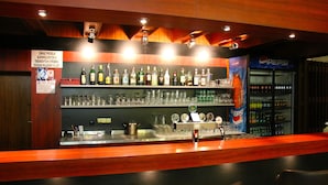Un espace bar avec des étagères remplies de bouteilles d’alcool, de verres et un réfrigérateur contenant des boissons Pepsi.