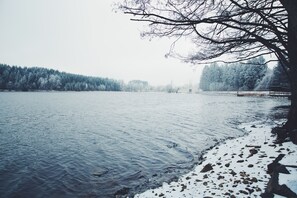 A calm lake with snow on the shore and trees in the background.