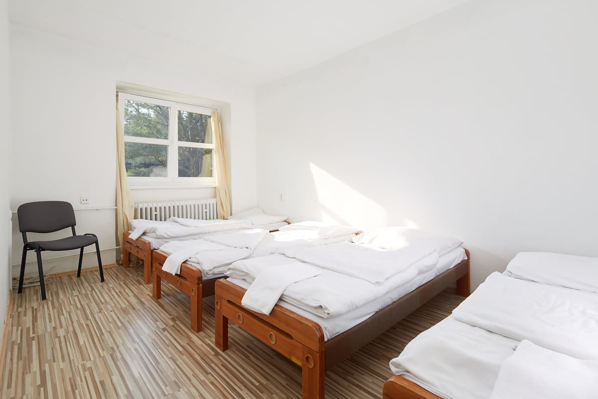 A room with three wooden beds, a chair, and a window with curtains.