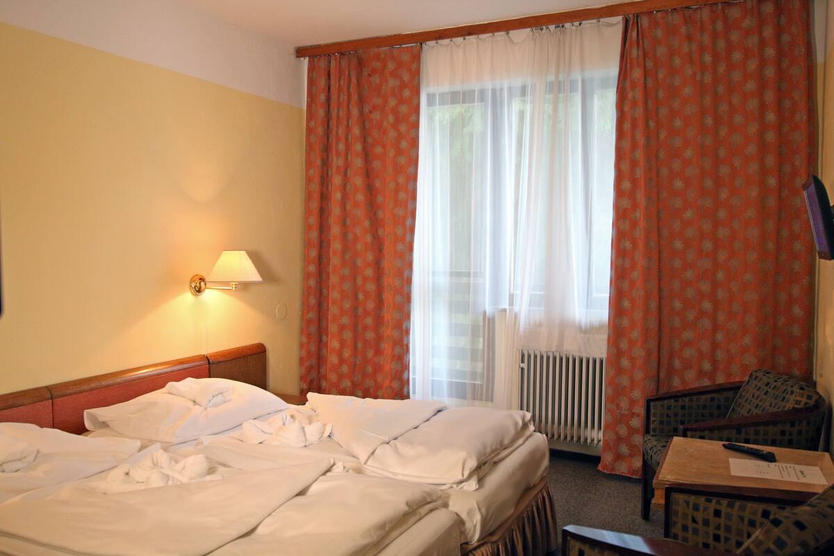 A hotel room with a bed, a chair, a table, a lamp, and a window with curtains.