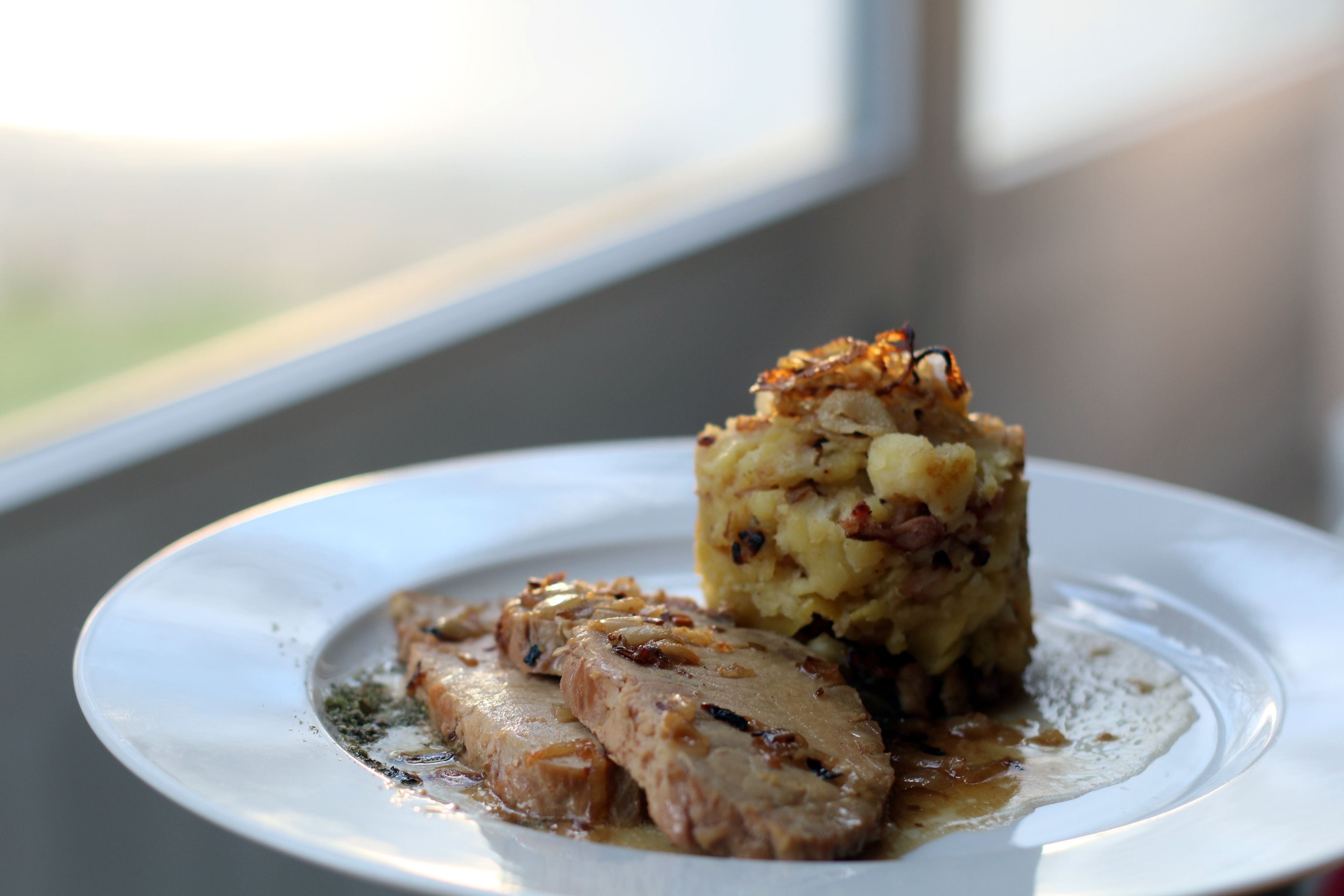 A plate with a slice of meat and a mound of mashed potatoes topped with nuts.