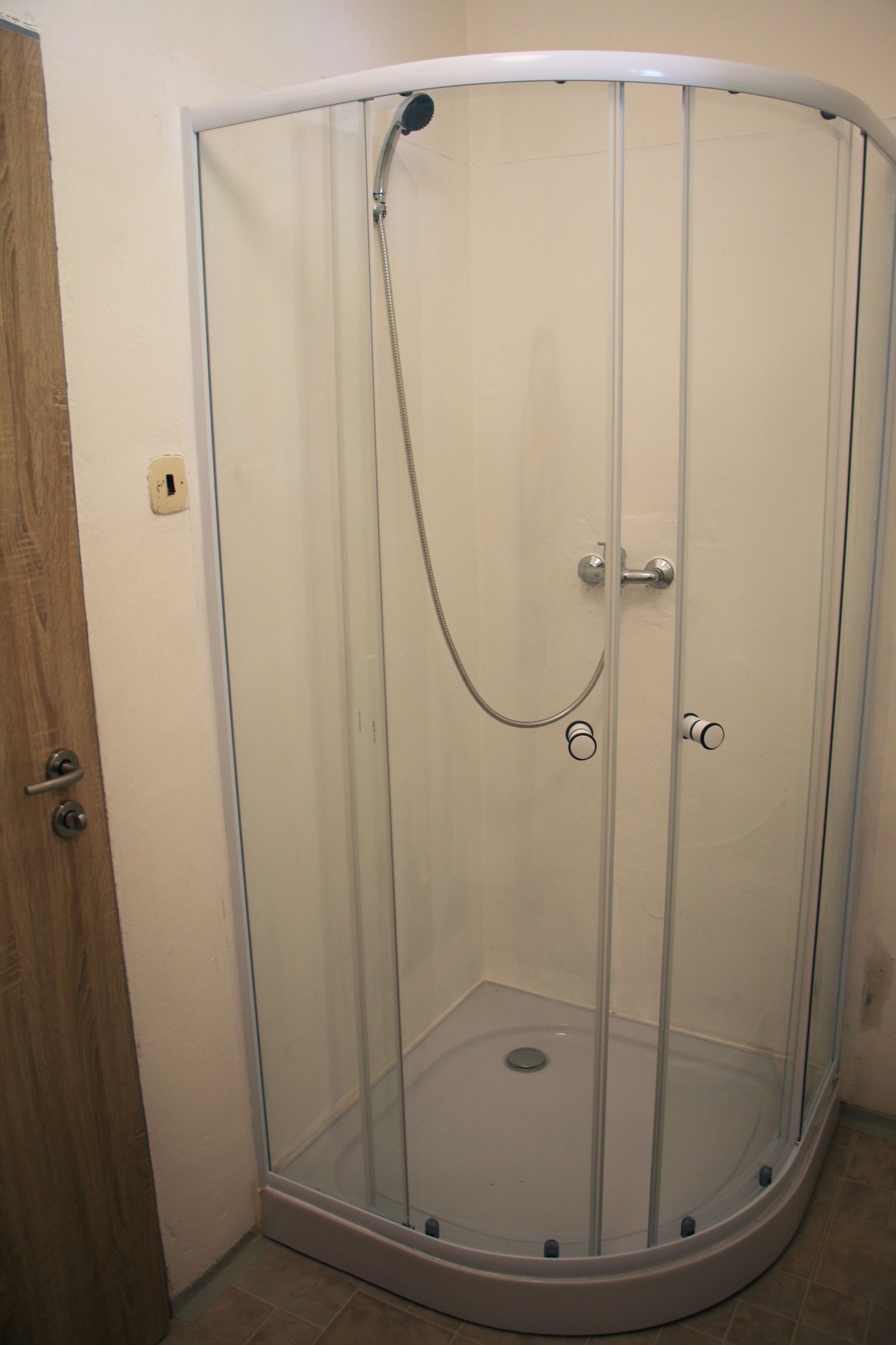 A glass-enclosed shower stall with a showerhead and control knobs.