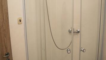 A glass-enclosed shower stall with a showerhead and control knobs.