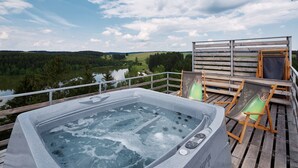 Un bain à remous sur une terrasse en bois, avec vue sur un lac et une forêt.