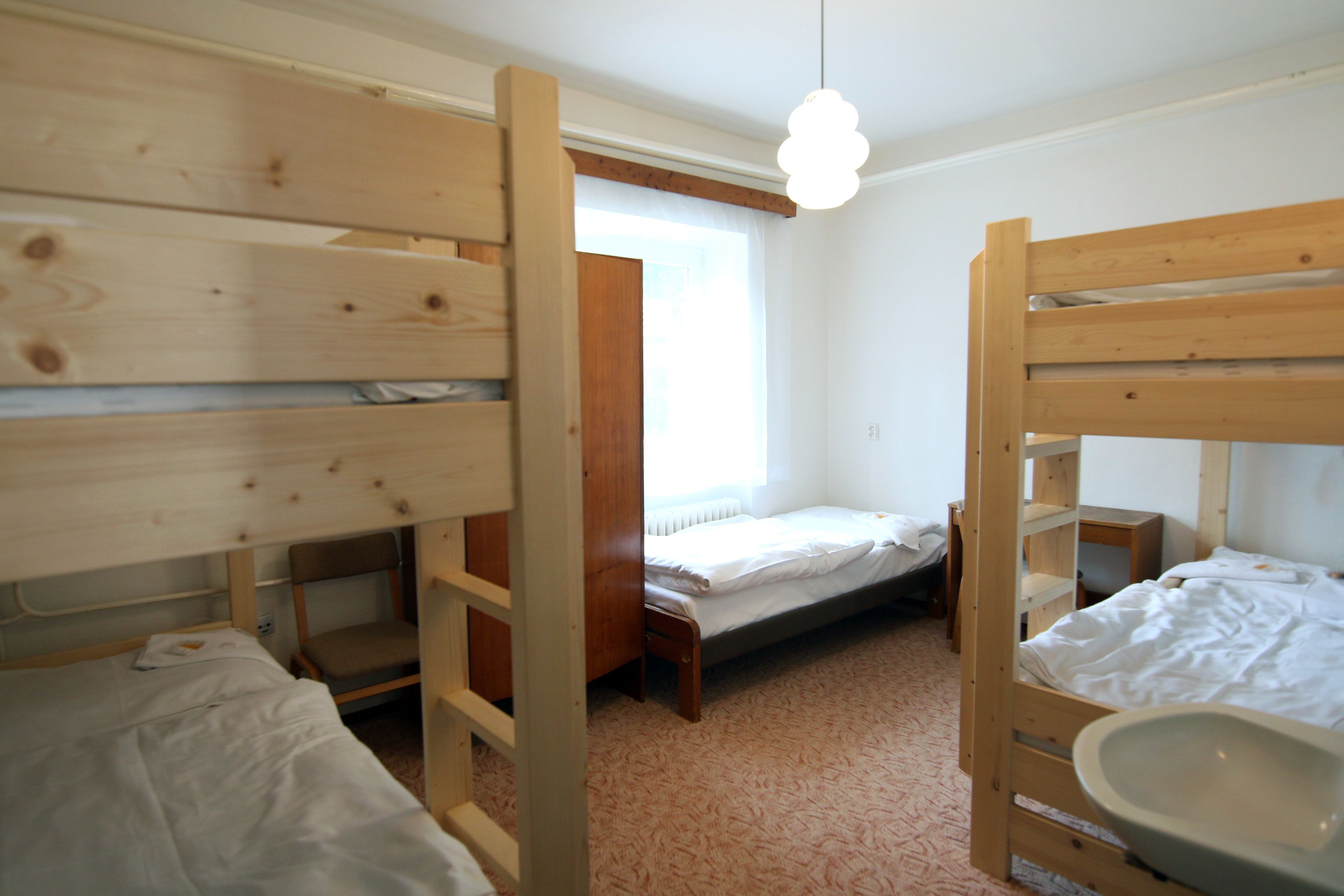 Habitación con literas de madera, una cama individual, una silla de madera, una mesita pequeña y una lámpara colgante.