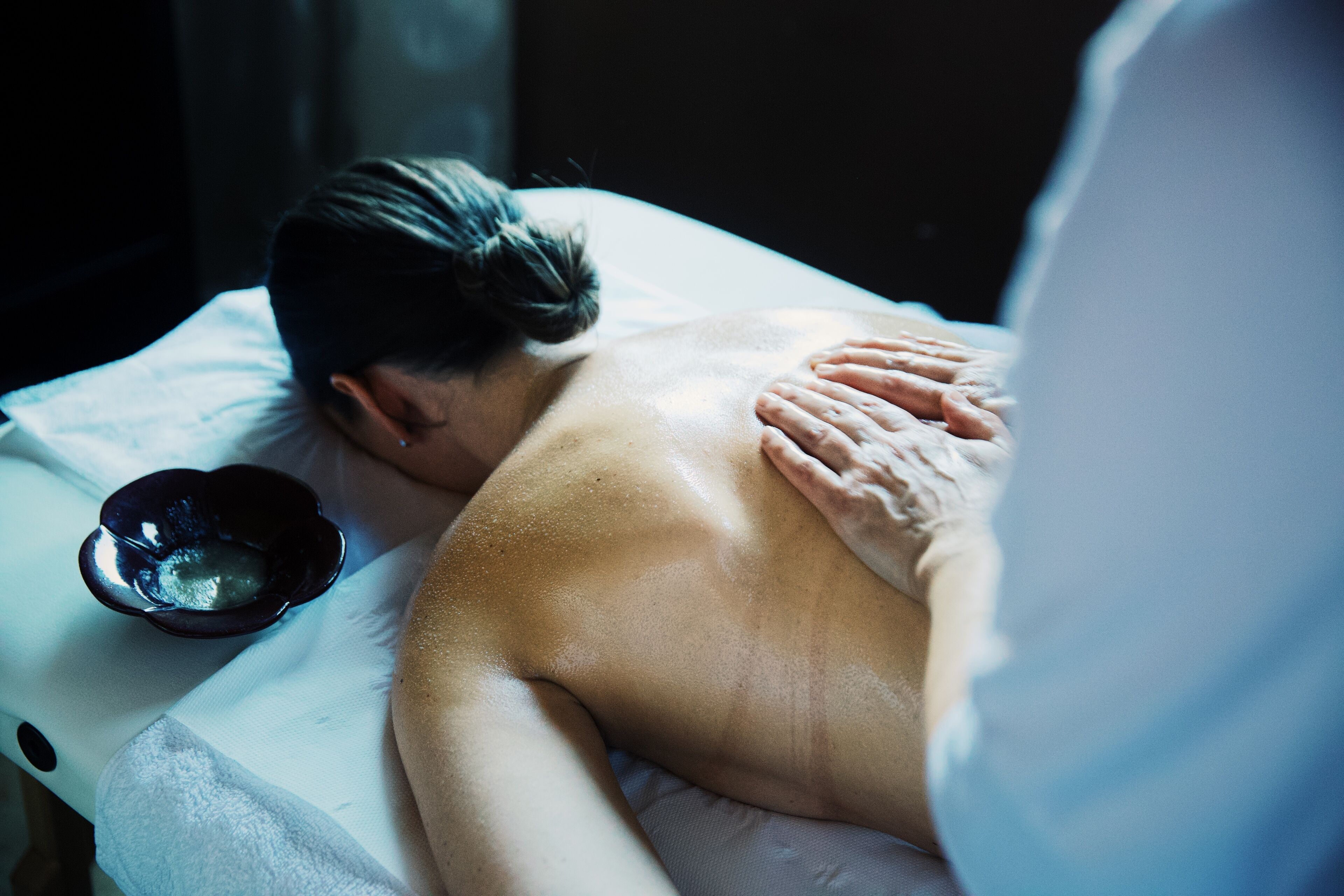 A person receiving a massage on a massage table with a towel and a small bowl.