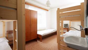 A room with bunk beds, a wooden wardrobe, a single bed, a bedside table with a television, and a bathroom with a sink and mirror.