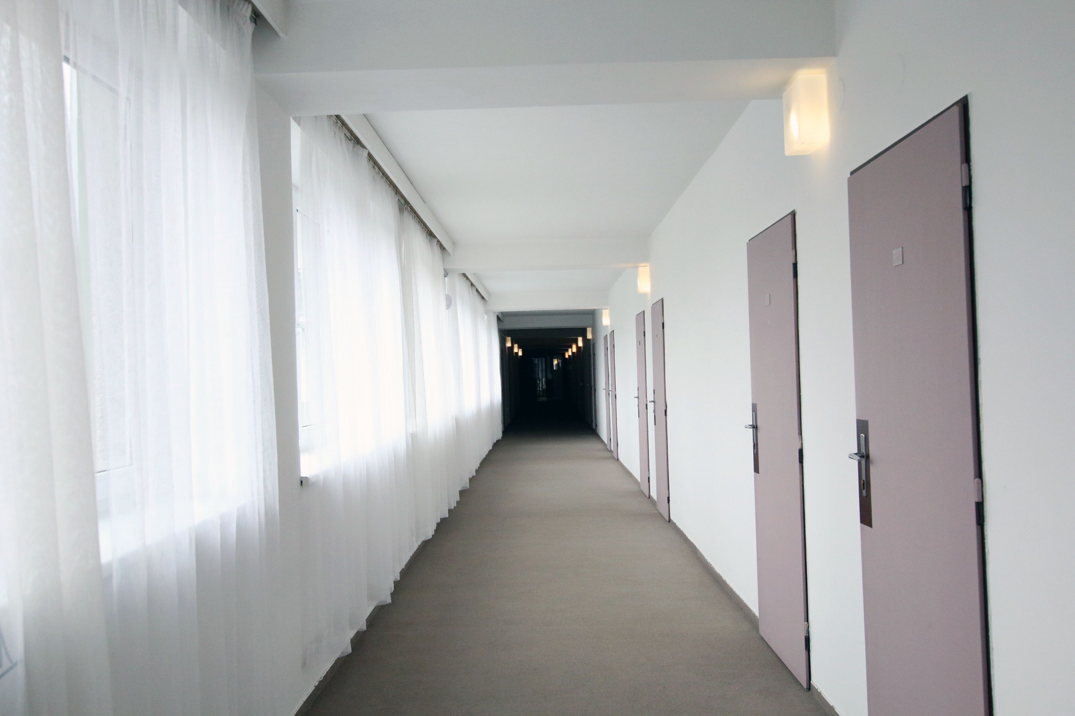Un long couloir étroit, doté d’un sol recouvert de moquette, de murs blancs et de portes d’un seul côté.