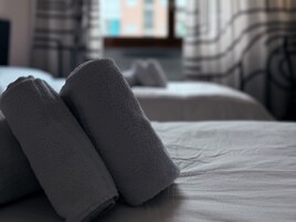 Un letto rifatto con due asciugamani piegati e una finestra ben visibile sullo sfondo.
