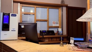 A hotel reception desk with a clock, a cash register, a computer, and a telephone.