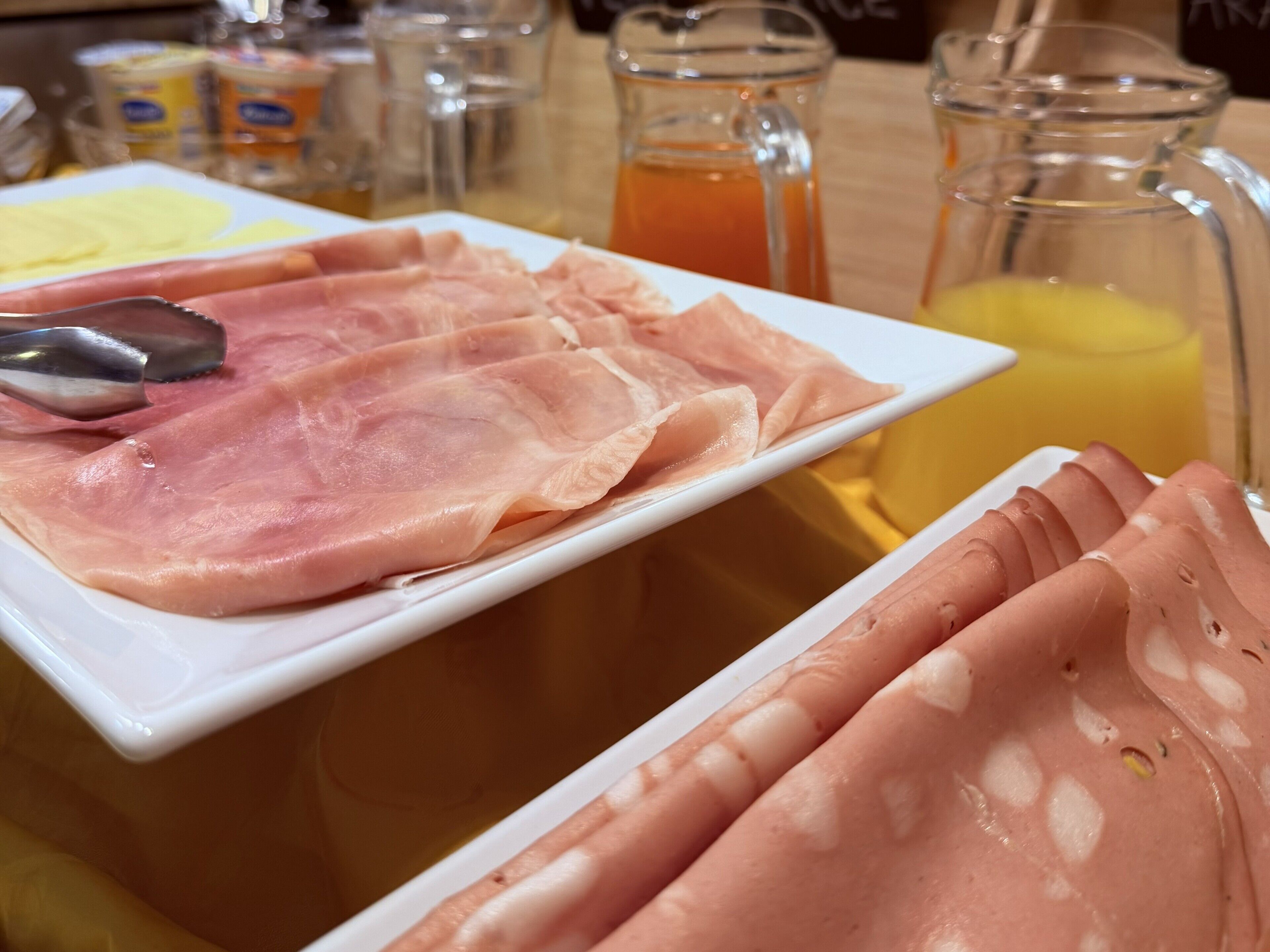 A breakfast buffet with sliced ham and a pitcher of orange juice.