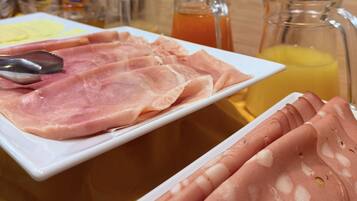 A breakfast buffet with sliced ham and a pitcher of orange juice.
