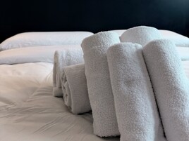 Asciugamani bianchi piegati ordinatamente su un letto con un piumone bianco liscio.