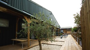 Une terrasse en bois avec un banc, un petit arbre et un bâtiment doté d’un toit en métal.