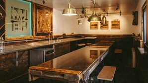Un long comptoir avec des tabourets, des luminaires suspendus et un meuble en bois servant de vitrine.