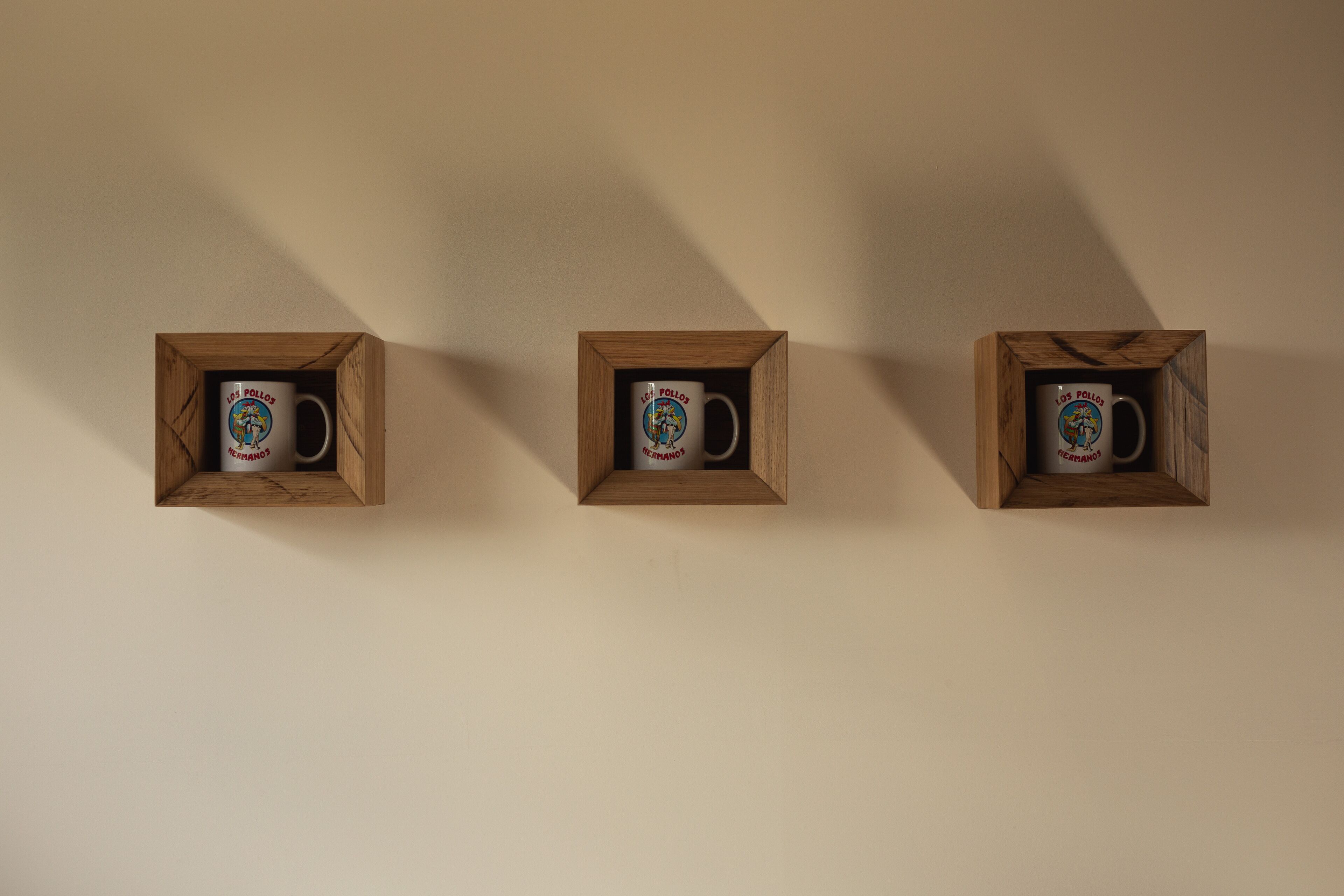 Tres vitrinas de madera con tazas sobre una pared lisa.