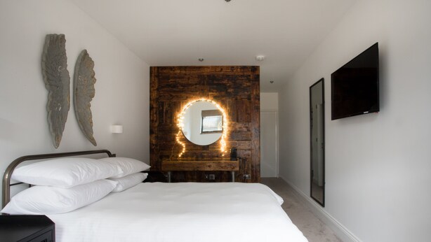 Une chambre à coucher avec un lit, une tête de lit en bois, un miroir et un téléviseur fixé au mur.
