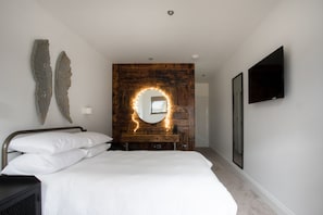 Un dormitorio con cama, cabecera de madera, espejo y televisor en la pared.