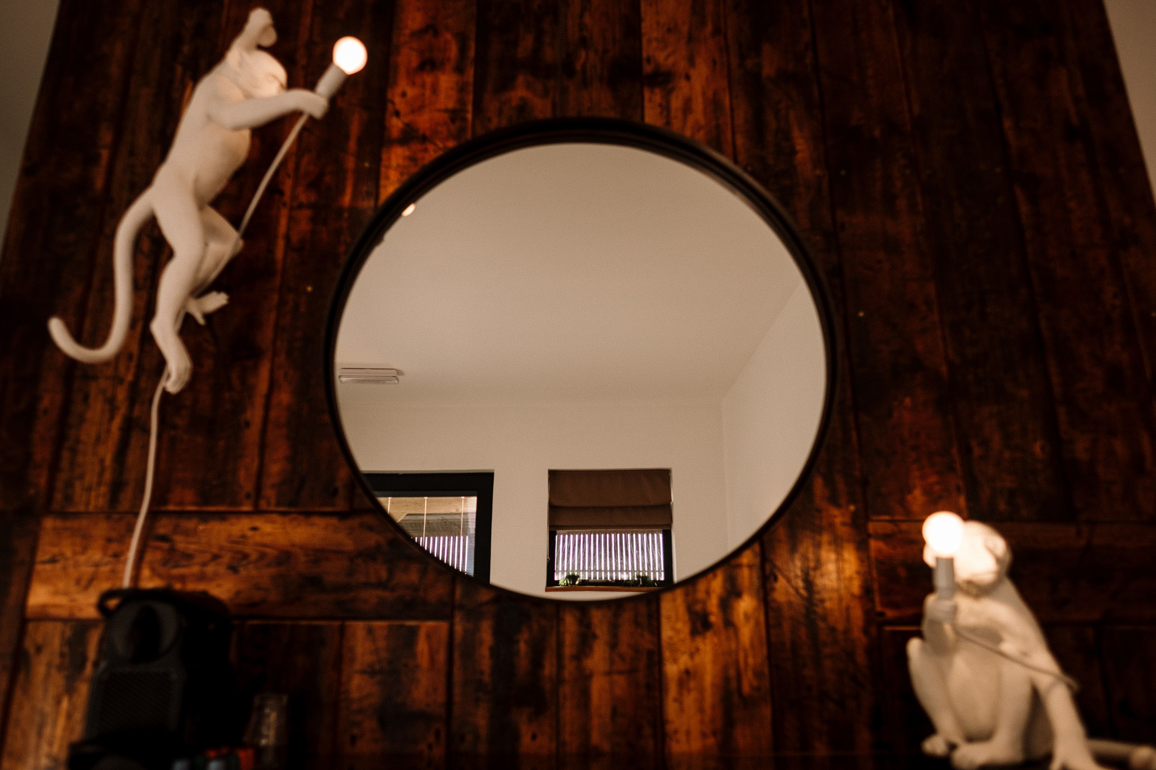 A round mirror on a wooden wall with two white statues, one holding a light and the other sitting.