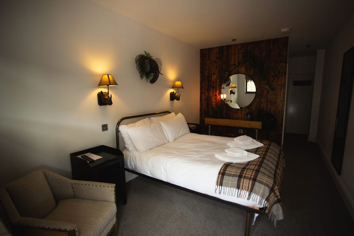 A hotel room with a bed, two bedside lamps, a chair, a mirror, and a wooden wall panel.