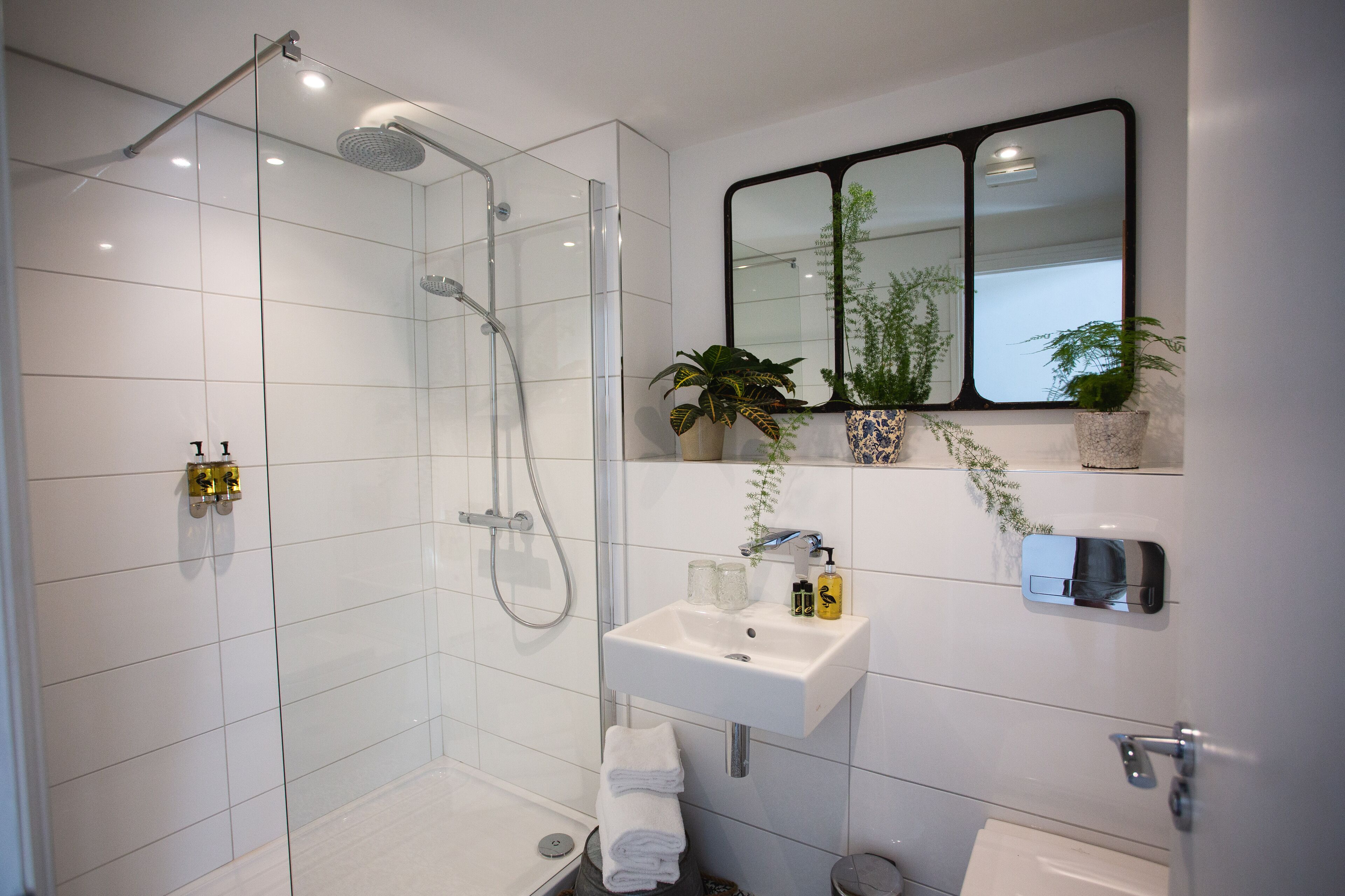A modern bathroom with a glass-enclosed shower, a white sink with a mirror above it, and a toilet.