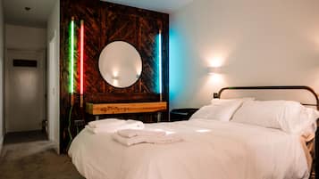 Habitación de hotel con una cama grande, un espejo redondo, un panel de madera decorativo y una mesita de noche con lámpara.